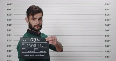 Karakolda fotoğraf çekilirken sakallı yakışıklı bir adamın yan profili. Şık saç kesimi olan, başını çevirip kameraya bakan bir erkek tutuklandı..