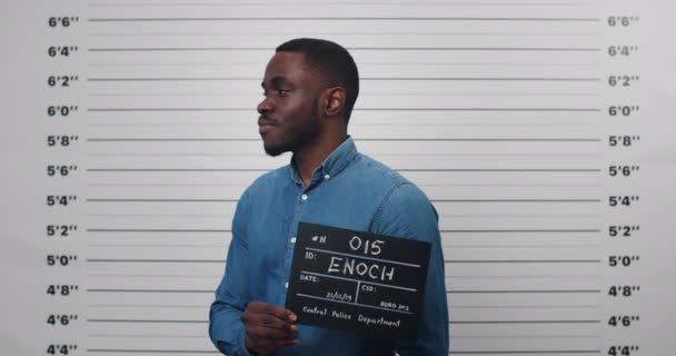 30 'lu yaşlarda Afro-Amerikalı bir adamın elinde tabela tutarken ve fotoğraf için poz verirken çekilmiş fotoğrafı. Polis departmanında kameraya bakan genç bir adamın görüntüsü. Suç kavramı. — Stok video