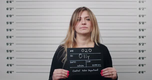Mugshot profil latéral d'une femme avec les cheveux teints soulevant la tête et regardant vers la caméra. Femme criminelle tenant signe pour photo tout en se tenant devant le mur d'alignement métrique de la police. — Video