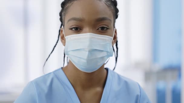 Tıbbi koruyucu maskeli bir kadının kameraya baktığı yakın plan görüntüsü. Hastanede rastalı poz veren genç bir kadın doktor portresi. Sağlık hizmeti kavramı. — Stok video