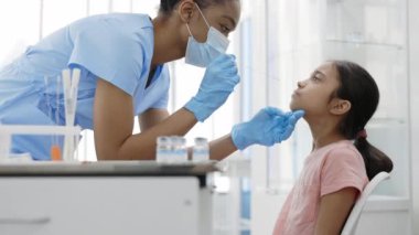 Koruyucu maskeli ve eldivenli tıbbi kadın çalışanın hastane odasındaki küçük bir kızdan PCR testi örneği alışının ekili görüntüsü. Covid araştırma ve tanı konsepti.