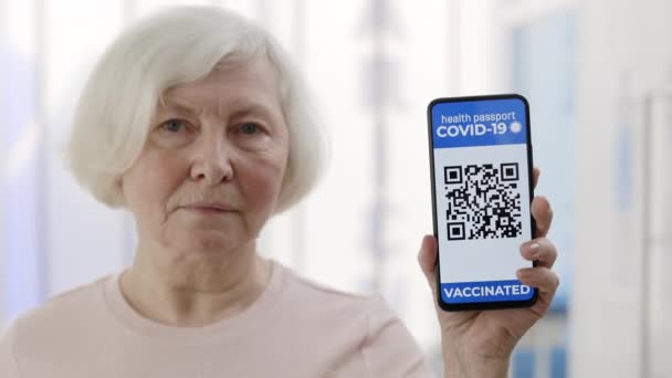 Γυναίκα ηλικιωμένη δείχνει στην κάμερα ένα smartphone με ανοσοποιητικό ψηφιακό διαβατήριο για covid-19. Κώδικας QR. Προβολή καλλιέργειας γυναίκας συνταξιούχος κάτοχος ψηφιακού διαβατηρίου εμβολιασμένου ατόμου. — Αρχείο Βίντεο