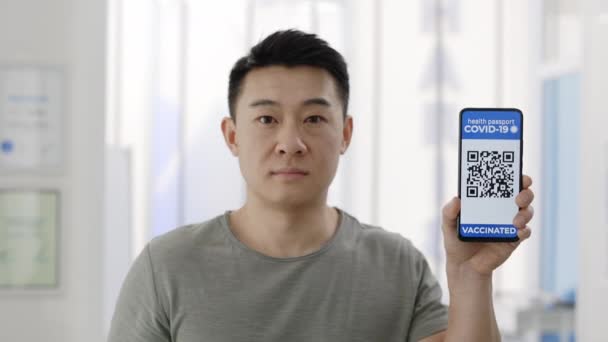 Pasaporte de vacuna digital. Hombre asiático mostrando teléfono inteligente en su mano con aplicación móvil para la vacunación. Vista de los cultivos del hombre adulto con pasaporte digital de la persona vacunada. — Vídeo de stock