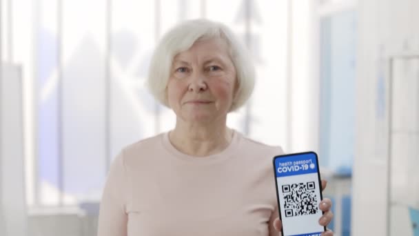 Ώριμη συνταξιούχος γυναίκα που δείχνει smartphone στο χέρι της με κινητή αίτηση για εμβολιασμό. Προβολή καλλιέργειας της συνταξιούχου γυναίκας που κατέχει ψηφιακό διαβατήριο εμβολιασμένου ατόμου. — Αρχείο Βίντεο