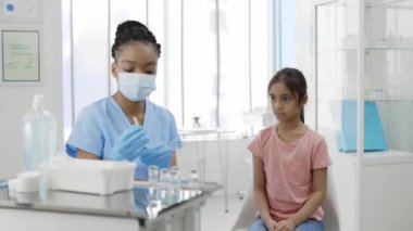 Aşı kabuğu 19. Hastane odasında koruyucu maskeli ve güvenlik eldivenli bir hemşire şırıngayı aşıyla dolduruyor. Aşı bekleyen küçük bir kız. Sağlık ve önleme kavramı.