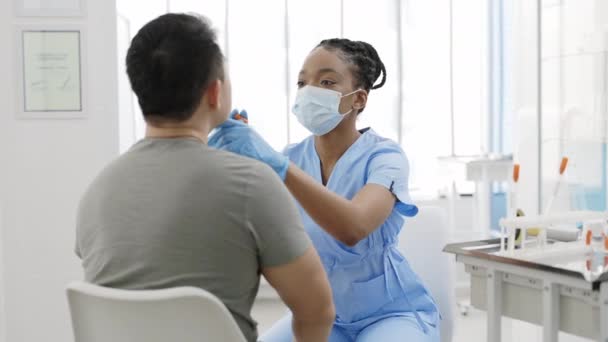 Ärztin mit Schutzmaske und Handschuhen, die im Krankenhauszimmer eine Probe des PCR-Tests aus dem Rachen eines männlichen Patienten entnimmt. Konzept der Covid Reaesearch und Diagnostik. — Stockvideo