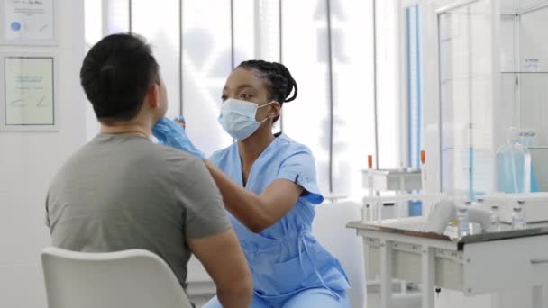 Schnittansicht einer Krankenschwester in Schutzmaske und Handschuhen, die im Krankenhauszimmer vor der Impfung eine PCR-Probe vom Mann entnimmt. Konzept der Covid Reaesearch und Diagnostik. — Stockvideo