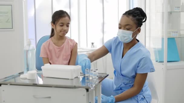 Ein kleines Mädchen schaut verängstigt, während eine Krankenschwester in Schutzmaske ihr einen Schuss COVID-19 Impfstoff gibt. . Konzept von Impfprogramm, Gesundheitsfürsorge, Prävention. — Stockvideo