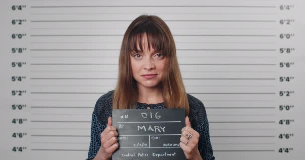Портрет дорослої жінки з передньою частиною, що тримає знак для фотографії в поліції. Погляд на красиву жінку-злочинця, що позує, піднімає голову і дивиться на камеру. Концепція куховарства . — стокове відео