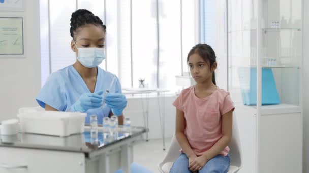Widok na małą dziewczynkę patrzącą jak pielęgniarka w masce ochronnej i rękawiczkach ochronnych wypełnia strzykawkę szczepionką w szpitalu. Koncepcja opieki zdrowotnej, szczepienia, profilaktyki. — Wideo stockowe