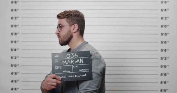 Duvarda duran sakallı ve bıyıklı adamın yan profili. Polis merkezinde fotoğraf çekilirken kameraya çevrilen gözlüklü bir erkek tutuklandı. — Stok video