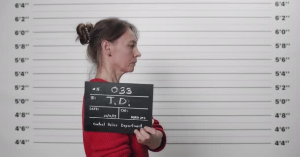 Een foto van een vrouw die gearresteerd is met een bord dat gefotografeerd werd. Portret van vrouwelijke crimineel op zoek naar camera in de politie bij lineup metric wall. — Stockvideo