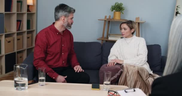 Женатая эмоциональная пара спорит, сидя в офисе психолога-женщины. Муж и жена ссорятся и обижаются перед женщиной-специалистом во время сеанса терапии. — стоковое видео