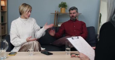 Married couple with relationship problems visiting family psychologist. Wife talking to counselor while her husband listening and try cheering her. Concept of family, marriage.