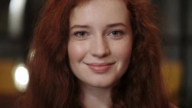 Kızıl saçlı, gülümseyen ve kameraya bakan genç bir kadının yakın görüntüsü. Mavi gözlü çekici bir kadın portresi. Pozitif duygu kavramı. Bulanık arkaplan.