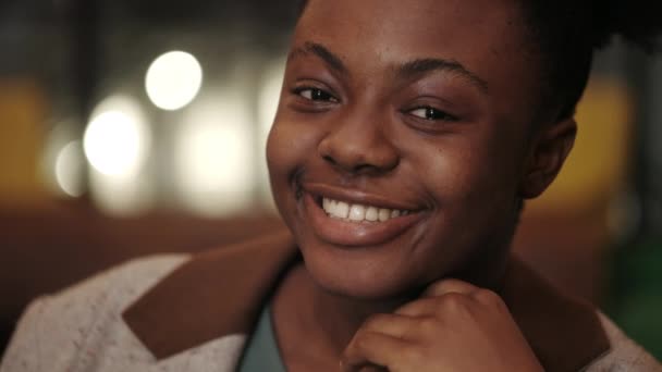 Заголовок молодої позитивної афро-американської жінки, яка тримає голову за руку, дивлячись на камеру. Портрет жінки, що кидає і сміється. Розмите тло. — стокове відео