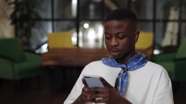 Afroamerikansk man får goda nyheter med mobiltelefon hemma. Chockad hane med öppen mun njuter smartphone kommunikation ser med förvåning på meddelandet på cellen. — Stockvideo