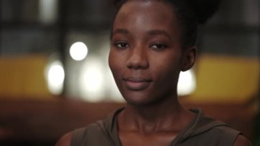 Genç Afro-Amerikan kadının gülümseyip kameraya bakarken başını çevirmesine yakından bakın. Güzel bir kadın pozu portresi. Vesikalık fotoğraf anlayışı. Bulanık arkaplan.