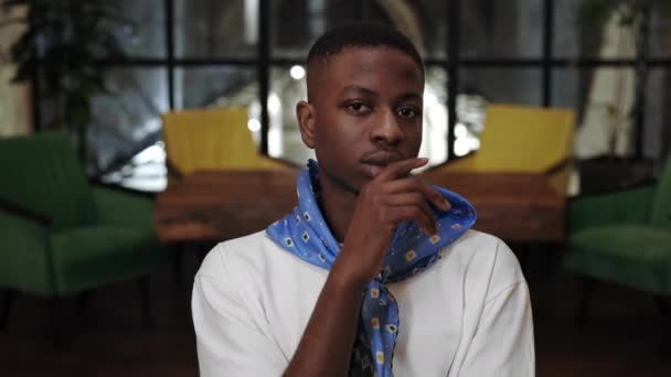 Crop view van jonge stijlvolle Afro-Amerikaanse man steunen en draaien hoofd terwijl op zoek naar camera. Portret van knappe man met halsdoek poserend in café. — Stockvideo