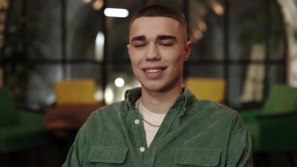 Crop view of millennial man with stylish haircut looking to camera. Portrait d'un beau jeune homme riant et posant assis dans un café. Fond flou. — Video