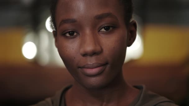 Vue rapprochée de la jeune femme afro-américaine souriante et regardant vers la caméra. Portrait d'une femme séduisante.Concept de headshot. Fond flou. — Video