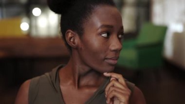 Genç, ciddi bir Afro-Amerikan kadının kameraya bakarken başını kaldırıp dönmesine yakından bakın. Kafede poz veren güzel bir kadın portresi. Bulanık arkaplan.