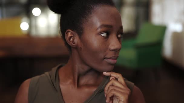 Vue rapprochée de la jeune femme afro-américaine sérieuse soutenant et tournant la tête tout en regardant à la caméra. Portrait de belle femme élégante posant dans un café. Fond flou. — Video