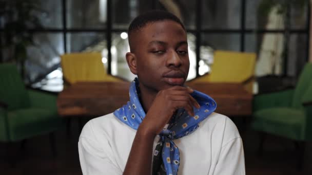 Vista de la cosecha de joven chico afro americano alegre apuntalando y girando la cabeza mientras mira a la cámara. Retrato de un hombre guapo con pañuelo posando y sonriendo en la cafetería. — Vídeo de stock