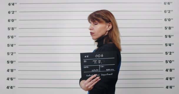 立っている間に逮捕された大人の女が頭を回してカメラを見ている。警察での写真のための40年代の女性犯罪者のミステリー・ビュー。犯罪の概念. — ストック動画