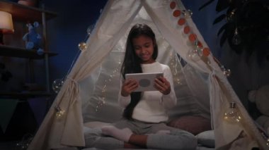 Güzel bir genç akşamları evdeki dekoratif derme çatma kulübede vakit geçiriyor. Tablette oynarken yerde oturan uzun siyah saçlı dikkatsiz kız. Boş zaman kavramı. .