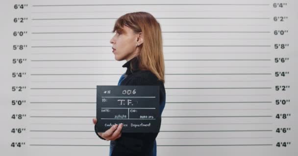 Mugshot einer erwachsenen Frau mit gefärbten Haaren, die sich zur Seite dreht, während sie ein Schild hält und für ein Foto posiert. Konzept des Verbrechens. — Stockvideo