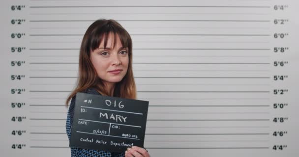 40 'lı yaşlarda tutuklu bir kadının fotoğrafı başını çeviriyor ve kameraya bakıyor. Polis departmanında elinde fotoğraf tabelası olan bir kadın suçlu.. — Stok video