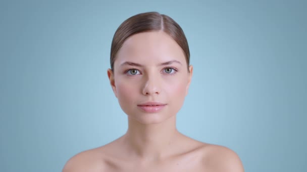 Vista de colheita de bela jovem mulher abrindo os olhos e olhando para a câmera. Retrato de mulher atraente com ombros nus e luz nua compõem posando no fundo do estúdio. — Vídeo de Stock