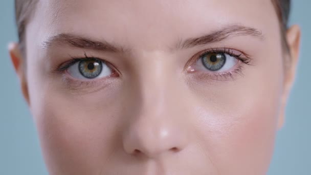 Close-up zicht op aantrekkelijke jonge vrouw gezicht openen ogen en op zoek naar camera. Portret van mooie vrouwelijke persoon met licht naakt make-up poseren op studio achtergrond. — Stockvideo