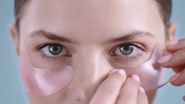 Nahaufnahme einer jungen Frau, die rosa Augenklappen aufsetzt, während sie in die Kamera blickt. Porträt eines weiblichen Models mit nacktem Make-up. Konzept der Haut- und Gesichtspflege. — Stockvideo