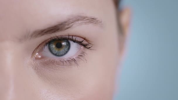 Close-up zicht van aantrekkelijke jonge vrouw gezicht half openen oog en op zoek naar camera. Portret van mooie vrouwelijke persoon met licht naakt make-up poseren op studio achtergrond. — Stockvideo