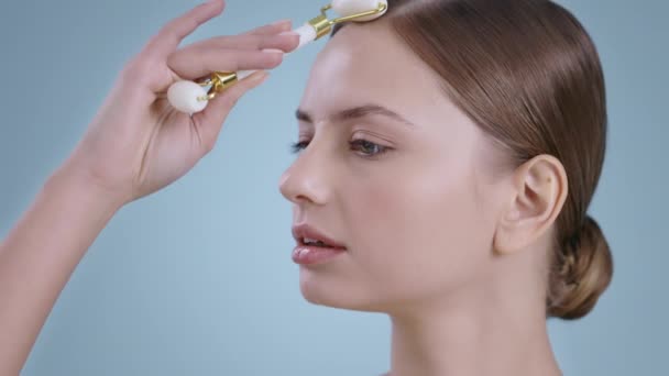 Portrait of pretty woman using facial massage roller for massaging nose and forehead. Female millennial model with naked shoulders and light nude make up .Concept of skin and face care. — Stock Video