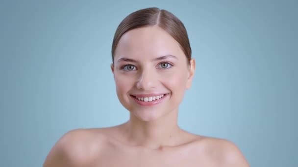 Close up de jovem mulher positiva com olhos azuis olhando para a câmera e sorrindo amplamente. Retrato de mulher bonita pessoa com ombros nus e luz nua compõem posando. — Vídeo de Stock