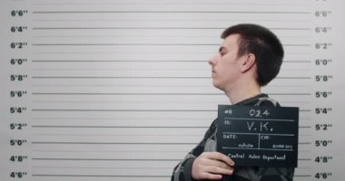 Yandan çekilen fotoğrafta erkek başını çevirip kameraya bakıyor. Polis metrik sıralama duvarının önünde dururken elinde fotoğraf tabelası tutan suçlu bir genç. Suç kavramı.