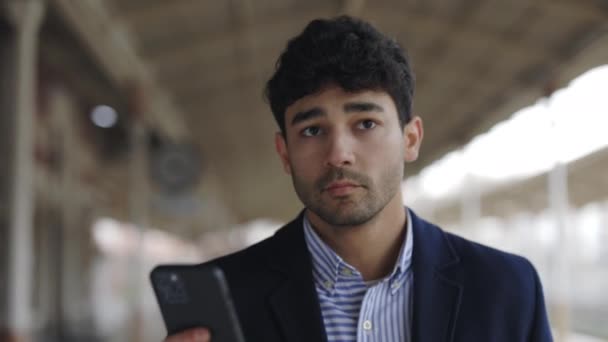 Retrato vista del ocupado hombre de negocios caminando por la estación de tren vacía y leyendo noticias en su teléfono inteligente mientras espera al tren — Vídeos de Stock