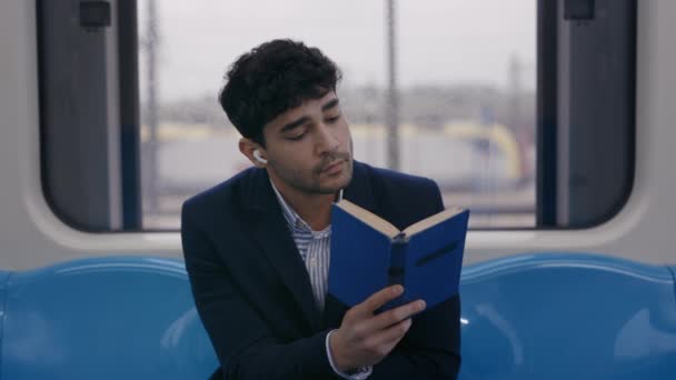 Людина в бездротових навушниках читає книгу в поїзді метро — стокове відео