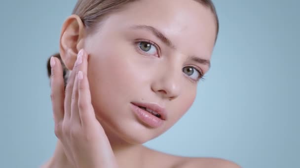 Hoofdfoto van een mooie duizendjarige vrouw die haar gezicht aanraakt terwijl ze naar de camera kijkt. Portret van vrouwelijk model met naakte schouders en naakt make-up poseren. Begrip kosmetologie en huidverzorging. — Stockvideo