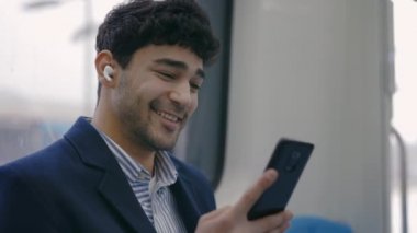 Kulaklıklı adam metroda akıllı telefon ekranına bakıyor.