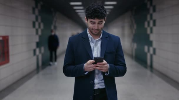 Gülümseyen adam, metro istasyonunda cep telefonuyla internette sohbet ediyor. — Stok video