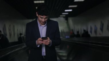 Yürüyen merdivende akıllı telefonu olan gülümseyen bir işadamı.