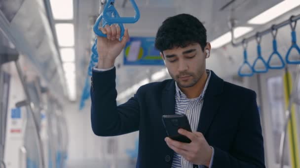 Metro yolculuğu sırasında akıllı telefon ve kulaklık kullanan bir adam. — Stok video