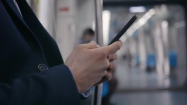 Genç adam metroda taşınırken akıllı telefon kullanıyor.