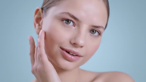 Hoofdfoto van een mooie vrouw die haar gezicht aanraakt terwijl ze naar de camera kijkt. Portret van vrouwelijk model met naakte schouders en naakt make-up poseren en glimlachen. Begrip kosmetologie, huidverzorging. — Stockvideo