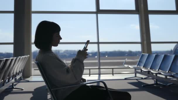 Fiatal nő ül a repülőtéren, és a modern okostelefon — Stock videók