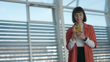 Havaalanında cep telefonuyla internette gezinen mutlu kadın.